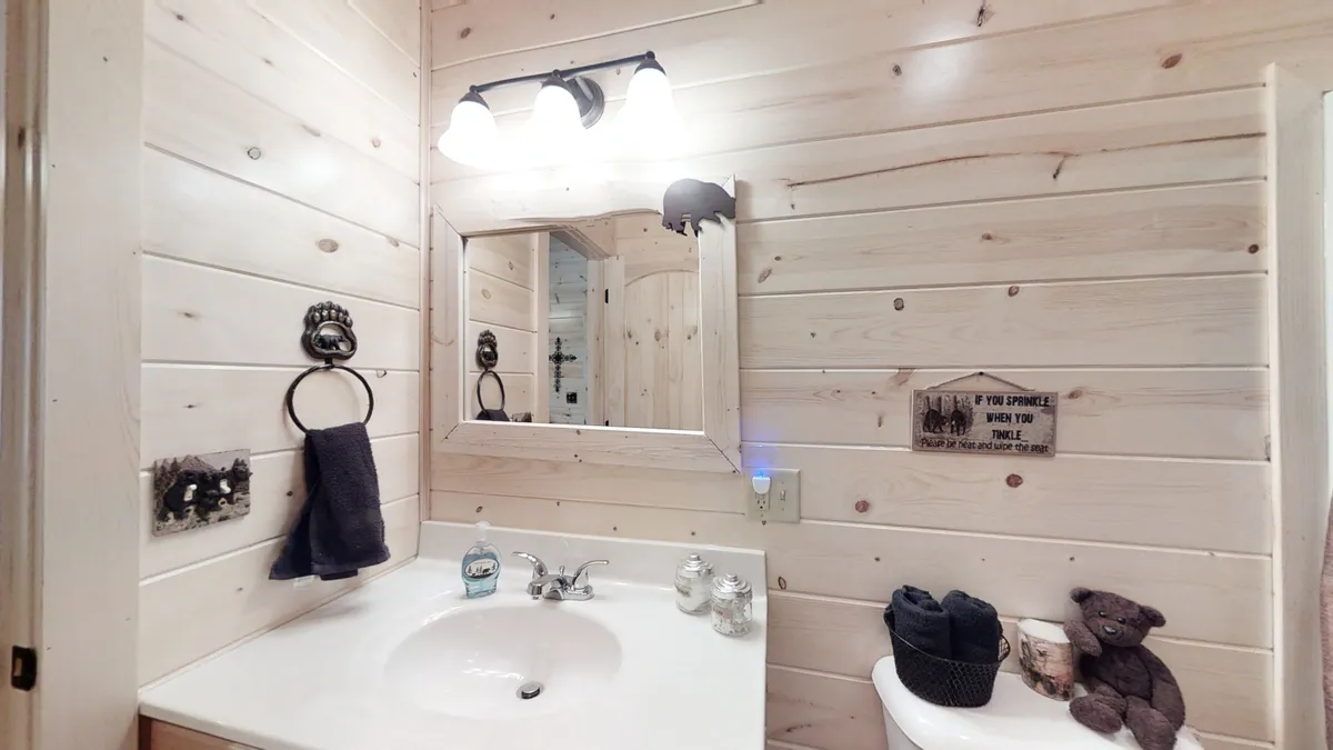 A bathroom scene with a well-lit vanity sink, mirror, decorative sign, plush towels, and a whimsical bear figurine. The atmosphere is inviting and perfect for morning or evening routines.