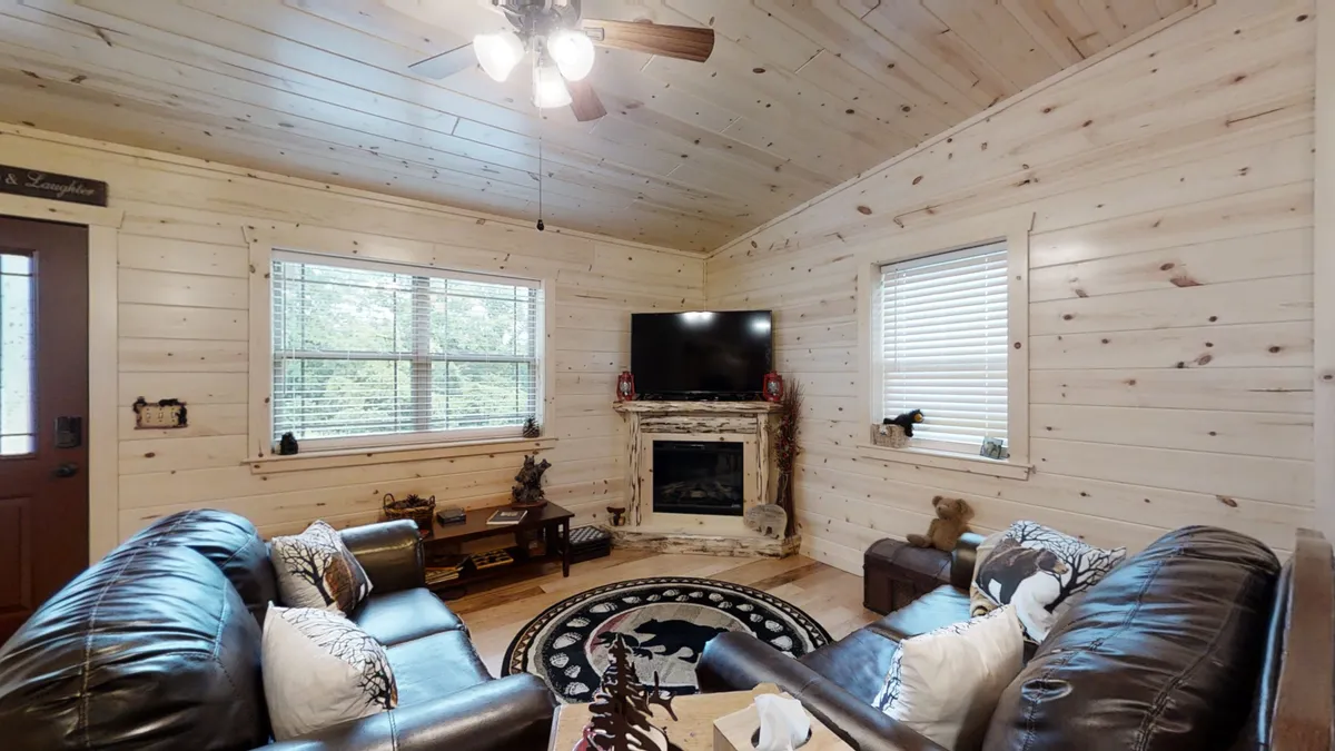 An inviting living space with leather sofas, a fireplace, a soft rug, and a TV. Natural light streams through the windows, illuminating the room and creating a welcoming setting for relaxing, socializing, and enjoying entertainment in any season.