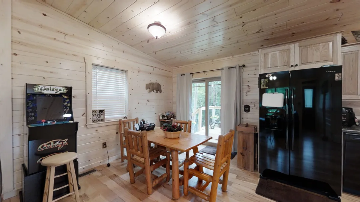 This image focuses on a cozy dining table adjacent to kitchen appliances, with a stand-up arcade machine close by. The setting is relaxed and family-friendly, highlighting spaces for shared meals and playful competition.