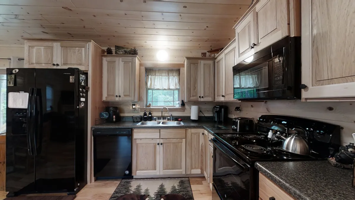 This inviting kitchen scene features black appliances, wooden cabinets, a sink with a window view, and a kitchen rug. The setup hints at a fully equipped and thoughtfully designed space for cooking, brewing coffee, and gathering with family.