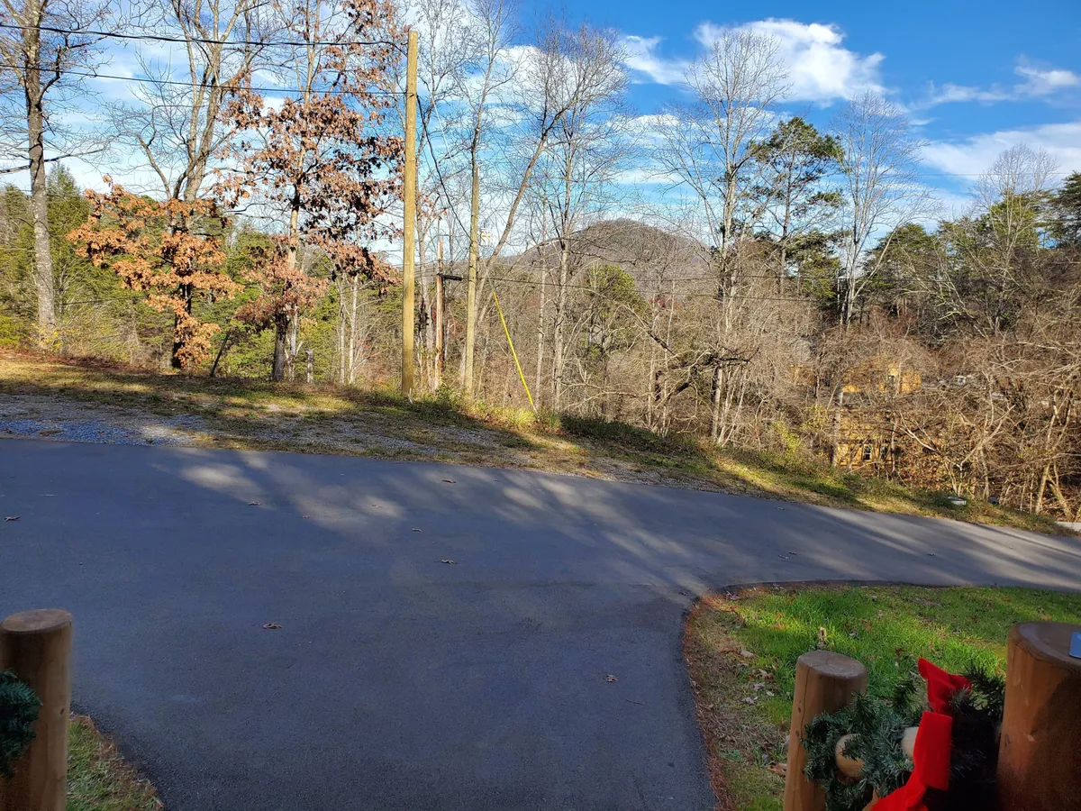 This image presents a scenic exterior view of the surrounding landscape, with a winding road, abundant trees, and a mountain backdrop. The tranquil, natural beauty of the setting is showcased, evoking a sense of escape and adventure.